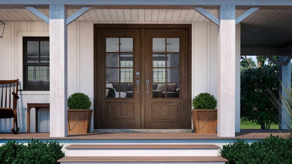 A wooden double door with glass panels, crafted by Relief Windows Baton Rouge, is elegantly flanked by potted shrubs, sitting atop a small porch adorned with white pillars and steps.