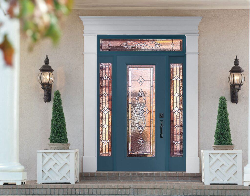 A teal front door with decorative glass panels from Relief Windows Covington, framed by white trim, flanked by two lantern-style lights and two potted topiary plants.