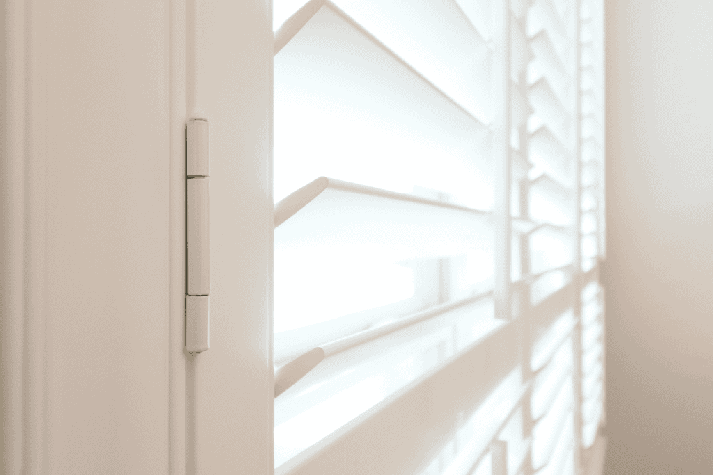 Close-up of white plantation shutters with light streaming through, highlighting the hinge on the left side, reminiscent of Relief Windows Beaumont craftsmanship.