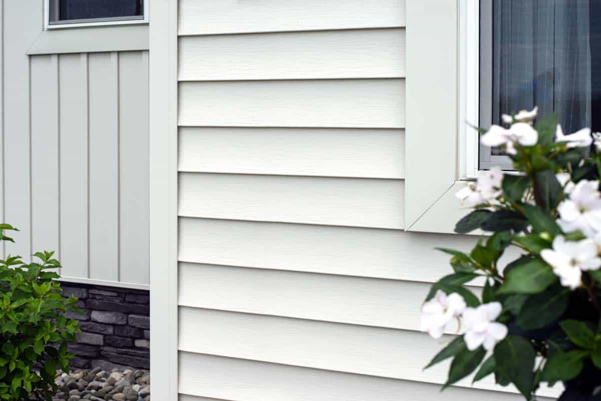 Close up of home with newly installed white siding with garden flowers in either side of view