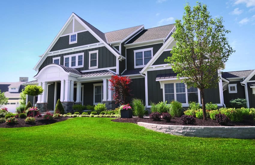 Large home with blue siding on a fresh green lawn, highlight by a clear blue sky