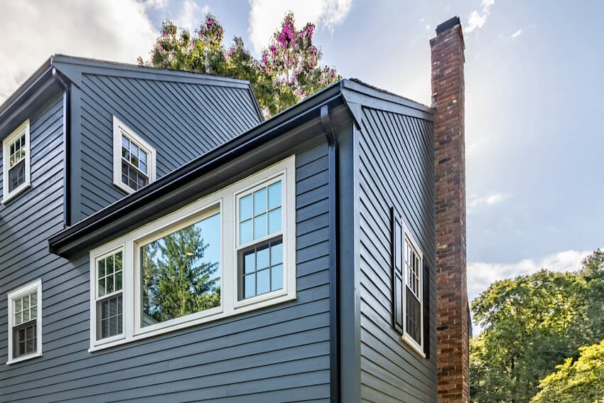 Tall, two-story home with blue siding and brick chimney up the side of the house