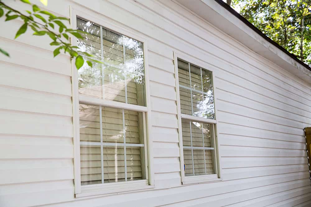 Angled view of home with white siding and white windows with green-leafed branches stretching in from the side of the frame
