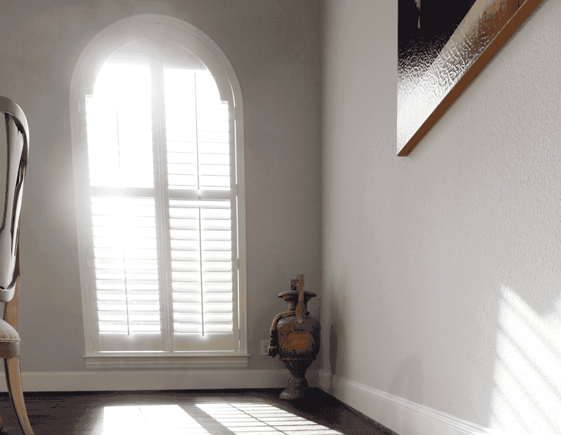 Arched windows with custom louvered interior window shutters with light streaming into hallway