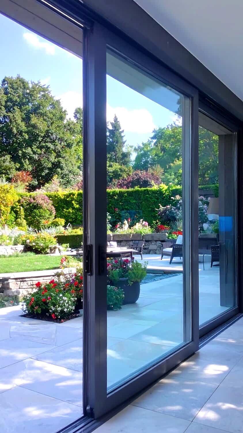 Black framed sliding glass doors looking out on a lush backyard garden