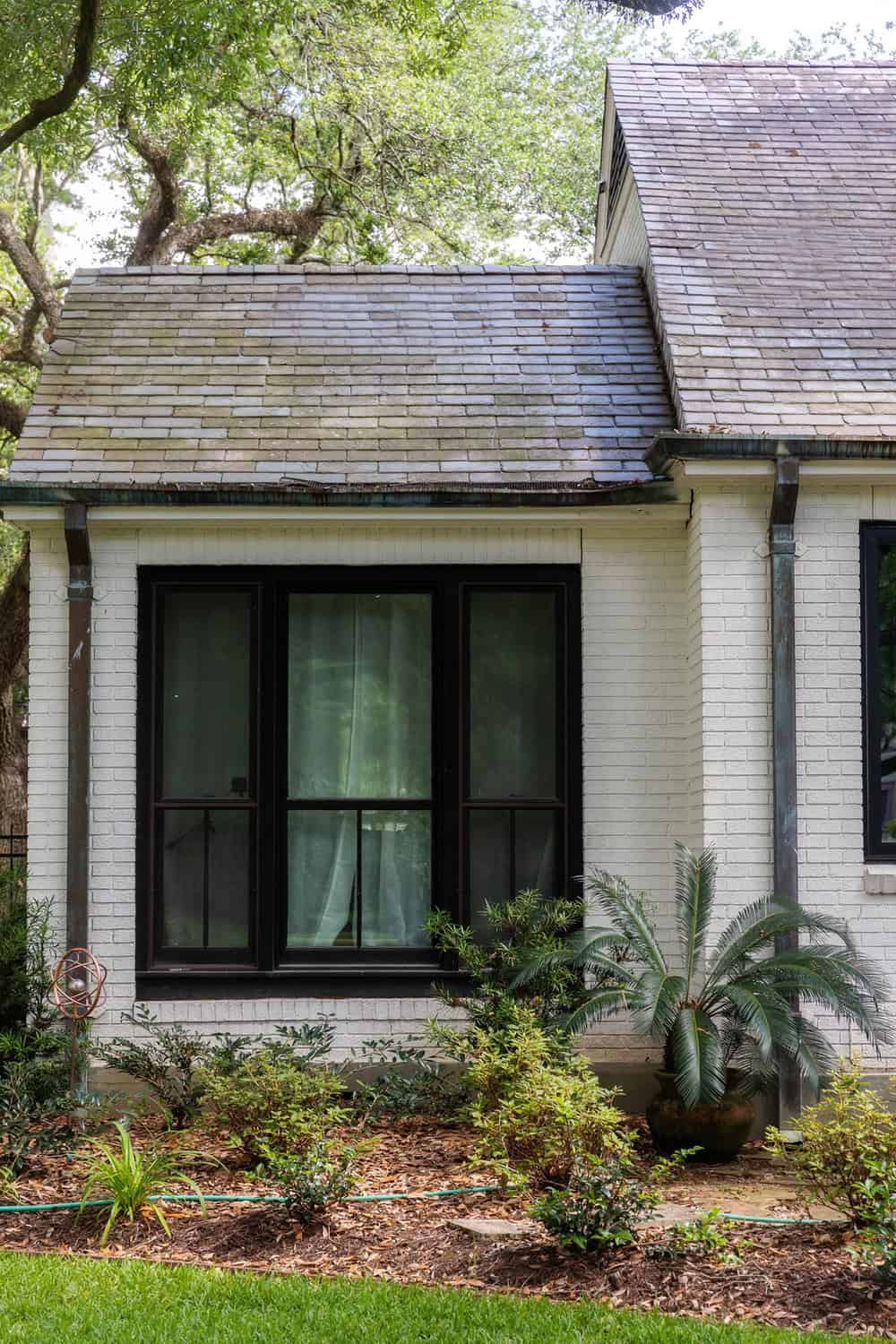 Home with black 3-lite end vent windows, white siding, and a shingle roof with plants growing out front